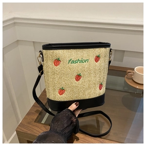 Close-up of strawberry embroidery and green fashion lettering on woven straw bucket bag