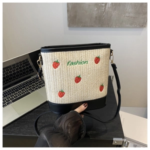 Close-up of strawberry embroidery and green fashion lettering on woven straw bucket bag