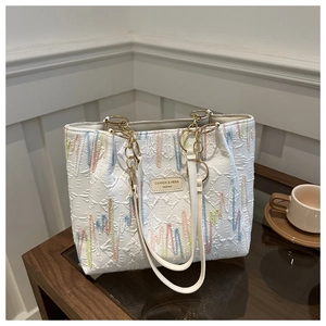 Bolso tote plisado blanco con bordado colorido y cadena dorada sobre mesa de madera