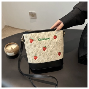 Straw bucket bag with strawberry embroidery and black leather strap shown from above