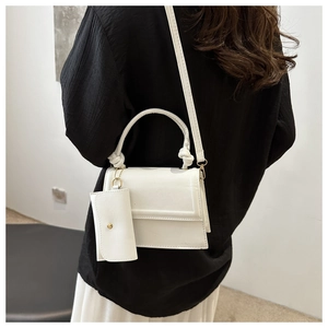 Detailed view of a white leather crossbody bag with knot handle and matching coin purse charm