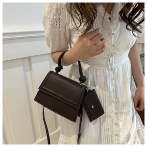 Close-up of chocolate brown square handbag with knotted handle and mini charm detail