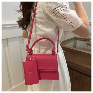 Detail of a bright fuchsia crossbody bag with knotted handle and matching mini pouch