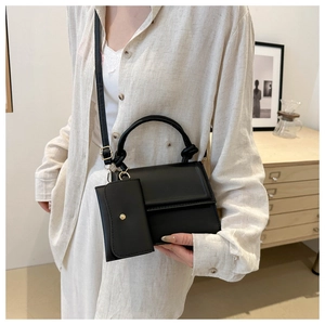 Detail of a minimalist black crossbody bag with knotted handle and matching mini pouch