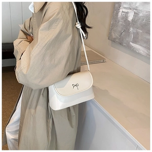 Detail of white leather shoulder bag featuring a black bow and knotted strap design