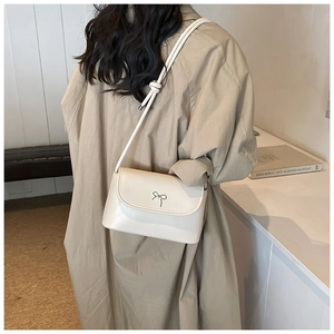 Side view of a cream crossbody bag with silver bow accent on a beige trench coat