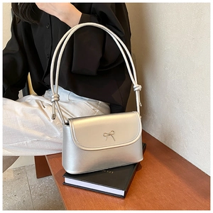 Close-up of a silver satin shoulder bag featuring a metallic bow and rope strap detail