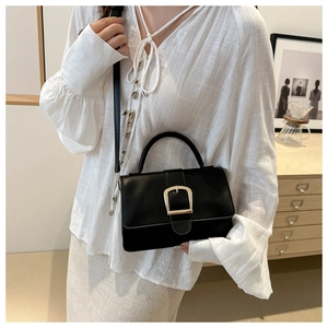 Détail d'un sac à main en cuir noir avec boucle dorée et poignée arrondie