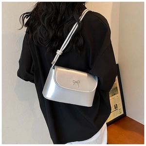 Detail of silver metallic handbag with bow accent worn over shoulder by a model