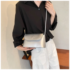 Detail view of a silver metallic crossbody bag with a cute bow clasp and slim shoulder strap
