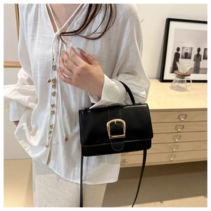 Détail d'un sac à main noir en cuir avec une grande boucle dorée et une poignée