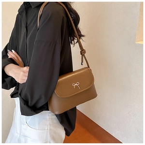 Close-up of brown leather shoulder bag with silver bow buckle and knotted strap detail