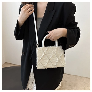 Detail of beige quilted denim crossbody bag with frayed edges and top handle