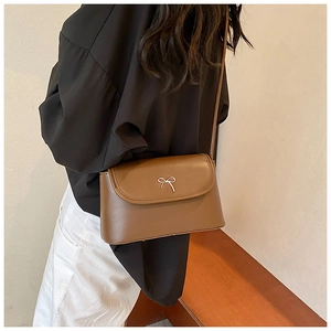 Brown leather crossbody bag with silver bow buckle worn by a model in a warm home setting