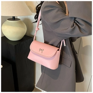 Detail of pink crossbody bag featuring a golden bow buckle and knotted shoulder strap