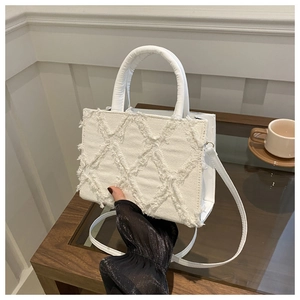 White quilted denim handbag with frayed edges and circular handle shown in a cafe setting