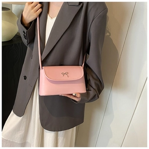Detail of pink leather crossbody bag with gold bow clasp worn by model in grey blazer