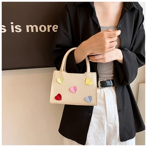 Detail of beige textured handbag featuring colorful heart patches and round handles