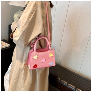 Pink woven crossbody bag with colorful 3D heart patches shown on a shoulder strap
