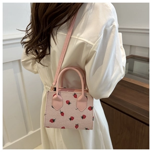 Pink straw tote bag with red strawberry pattern shown on model in natural light