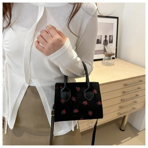 Detail of black corduroy tote with red strawberry embroidery and crossbody strap