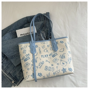 Dettaglio della borsa tote in PU crema con stampe graffiti blu su sfondo di tessuto bianco
