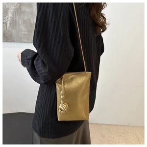 Detail of golden mini crossbody bag with metallic texture and large woven knot charm