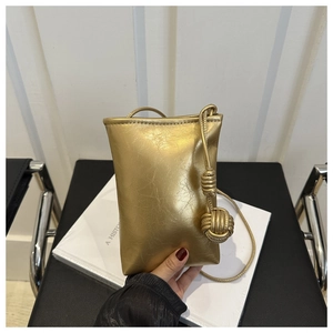 Detail of gold metallic mini crossbody bag featuring a textured finish and woven knot charm