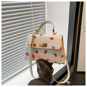 Close-up of beige corduroy handbag with strawberry print and gold twist lock