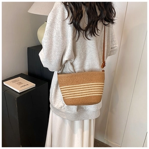 Side view of striped straw bucket bag with adjustable brown leather strap on model