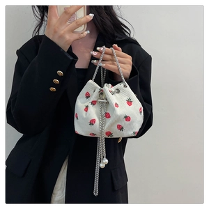 Close-up of white corduroy bucket bag with strawberry print and pearl chain detail
