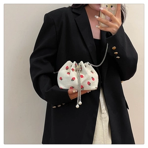 Detail of white corduroy bucket bag with strawberry pattern and pearl drawstring detail