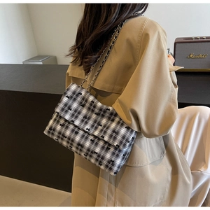 Detail of plaid crossbody bag with small bows and metal chain strap on trench coat
