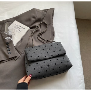 Detail of grey textured fabric bag with embroidered bow knots and metal chain strap