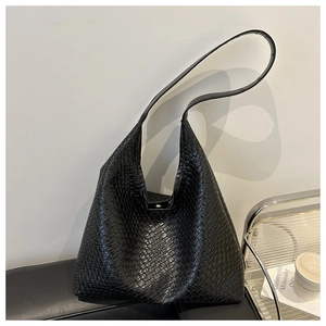 Close-up of a large black woven leather tote bag on a sofa with urban lifestyle props