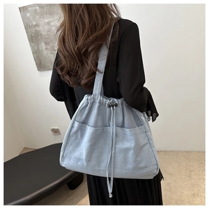 Light blue canvas tote bag with drawstring closure and front pockets shown on shoulder