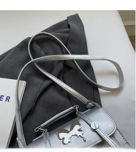 Détail du petit sac carré argenté avec logo papillon et bandoulière réglable