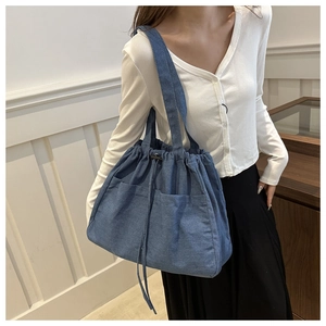 Detail of blue denim tote bag with drawstring closure and front utility pockets
