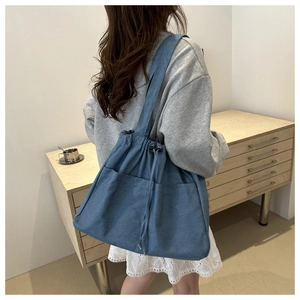 Detail of blue denim tote bag showing functional drawstring closure and two large front pockets