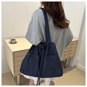 Large dark blue denim tote bag with drawstring closure and front pockets shown on model