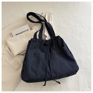 Detail view of large denim tote bag featuring dual front pockets and drawstring closure