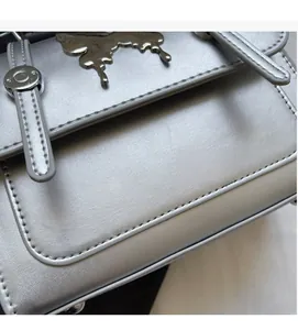 Détail d'un sac messager argenté métallisé avec pièce décorative en métal et surpiqûres