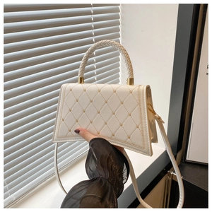 Dettaglio della borsa beige trapuntata con ricami a cuore d'oro e manico intrecciato