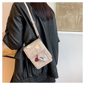 Chic beige denim square crossbody bag with colorful hearts and tassel worn by a model