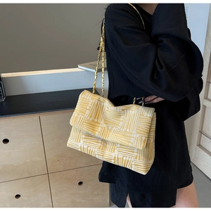 Detail of yellow woven crossbody bag featuring a metal chain strap and geometric patterns