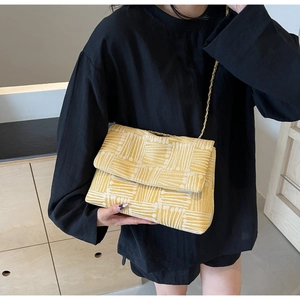 Detail of yellow and white woven cross-body bag with gold chain strap on black outfit