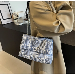 Detail of blue and white textured weave flap bag with gold chain strap on beige trench coat