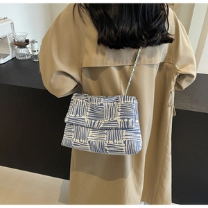 Close-up of woven blue and white striped shoulder bag with a gold chain strap