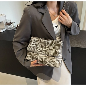 Detail of woven flap bag with coffee brown and cream patterns and metal chain strap