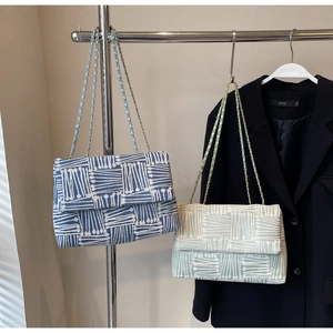 Detail of woven flap shoulder bags with metal chain straps in blue and green patterns